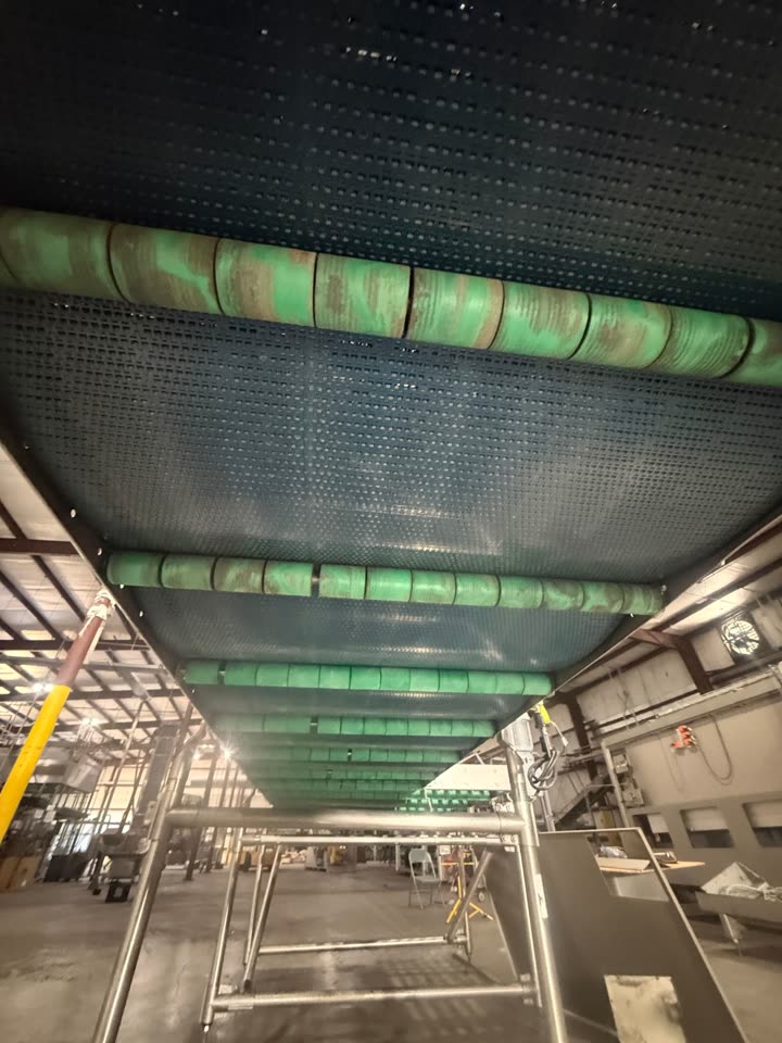 Underside of a modular plastic conveyor belt with residue on the green roller drums before dry ice blasting